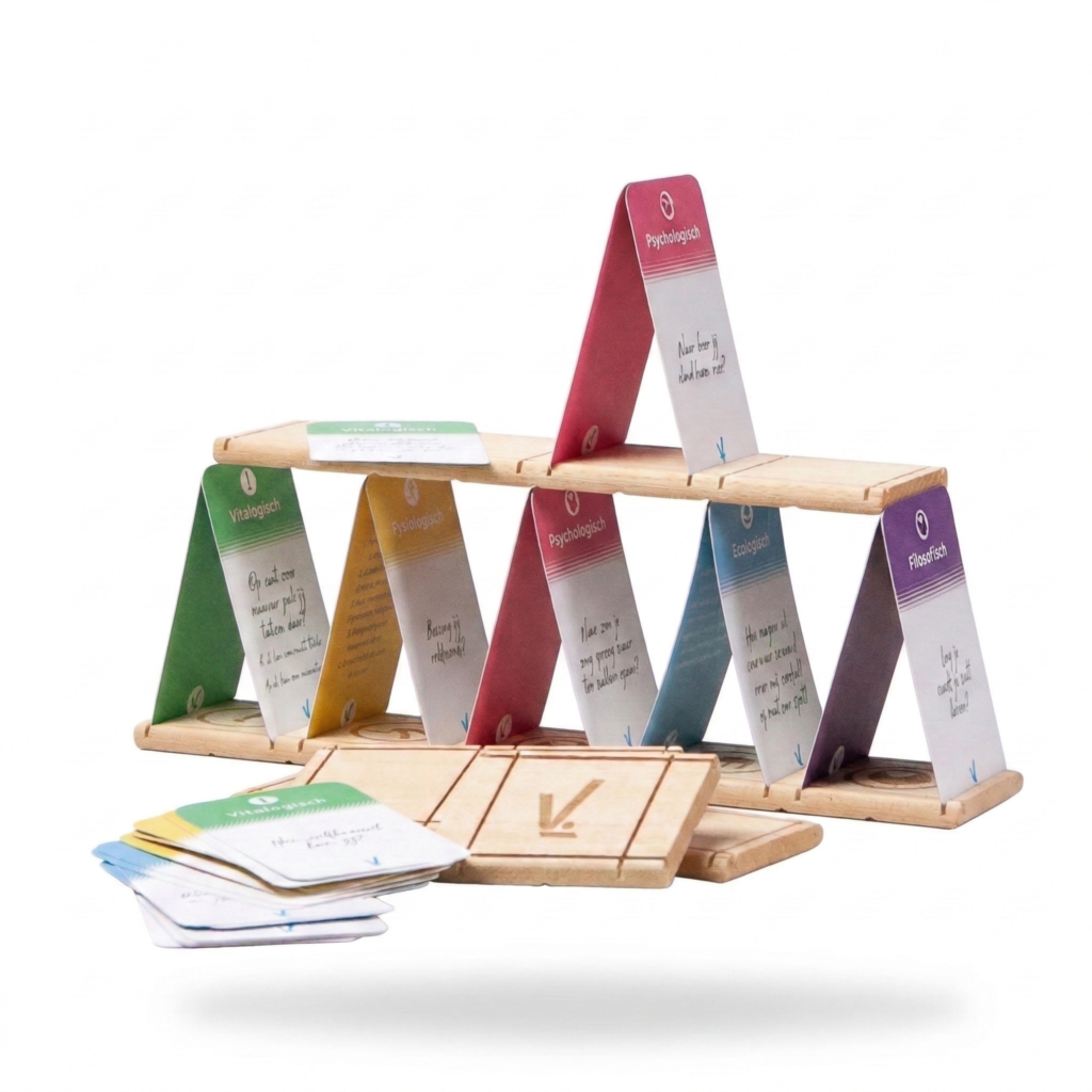 Een houten constructie in de vorm van een kaartenhuis, opgebouwd met gegraveerde houten plankjes en kleurrijke kaarten. De kaarten hebben verschillende categorieën zoals "Psychologisch", "Fysiologisch", "Ecologisch" en "Filosofisch", elk met een eigen kleur en reflectievraag.